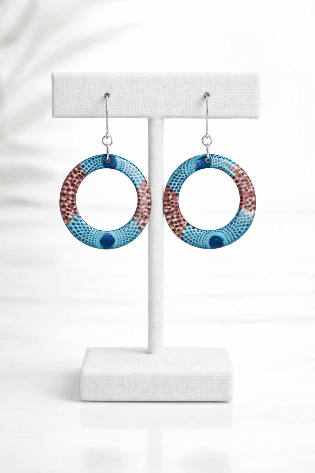 Blue mosaic-inspired hoop earrings displayed on a white jewelry stand with lightweight circular open-hoop design.